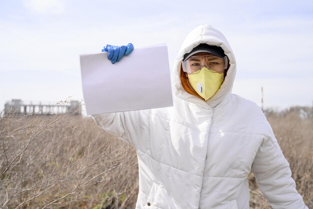 Foto retrato de mulher usando máscara segurando papel em branco enquanto está de pé em terra