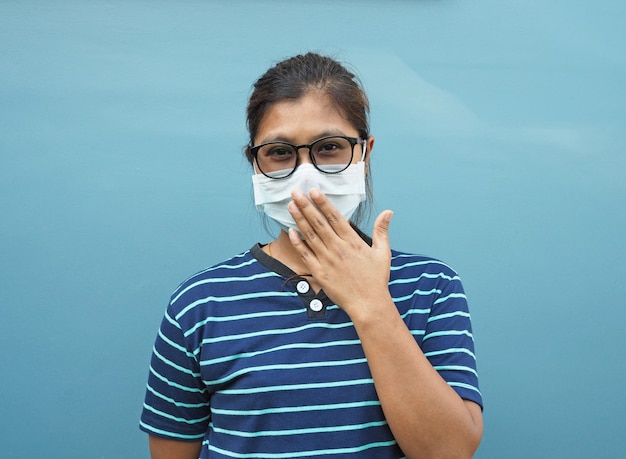 Retrato de mulheres asiáticas usando óculos e máscaras protetoras. enquanto cobre a boca em um fundo azul