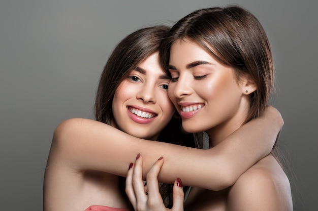 Retrato de mulheres gêmeas felizes com pele perfeita e maquiagem natural e cabelos longos. moda