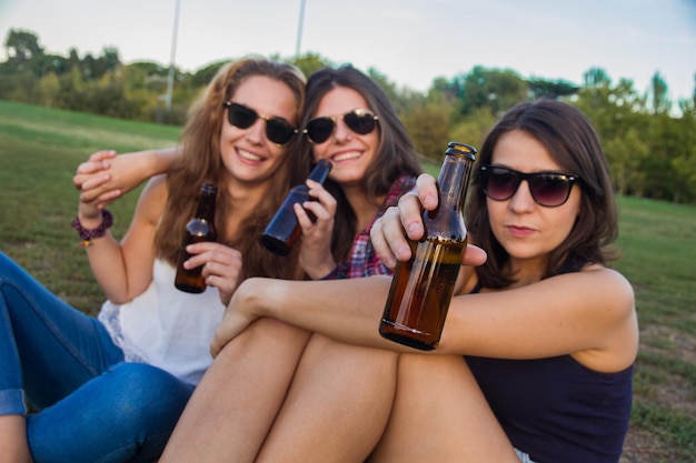 Foto retrato de mulheres jovens bebendo álcool enquanto estão sentadas no campo