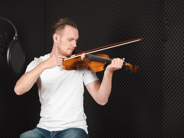 Retrato de músico bonito toca violino no estúdio de gravação