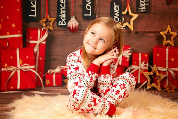 Retrato de Natal de um bebê feliz em pijama vermelho de Natal com um veado e a coroa no backgro.