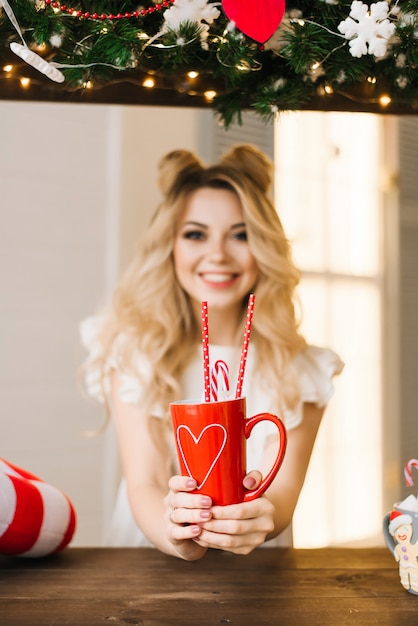 Retrato de Natal de uma menina bonita com uma caneca vermelha em uma barra de Natal. Ano novo e o conceito de Natal. Foco seletivo