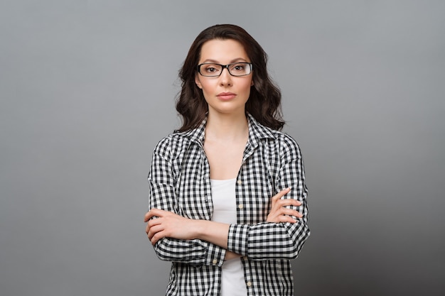 Retrato de negócios de uma jovem morena encantadora de óculos olha para a câmera que a cruza