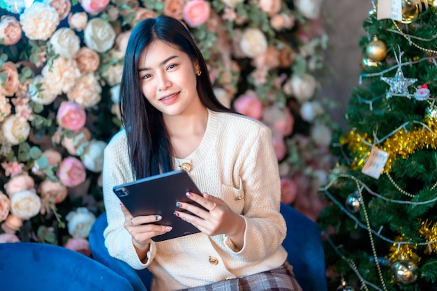 Retrato de negócios freelance belo sorriso positivo jovem mulher asiática trabalhando on-line com o uso de tablet Decoração Durante o Natal Natal e feriados de Ano Novo em casa no quarto dentro ou café