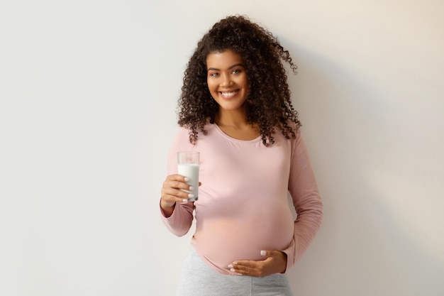 Retrato de nutrição da gravidez de mulher grávida negra sorridente com um copo de leite