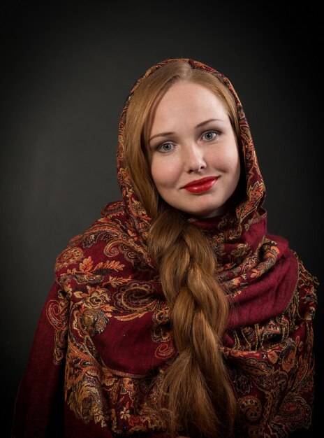 Retrato de olhar para a câmera e sorridente garota eslava com fundo escuro de cabelo trançado vermelho