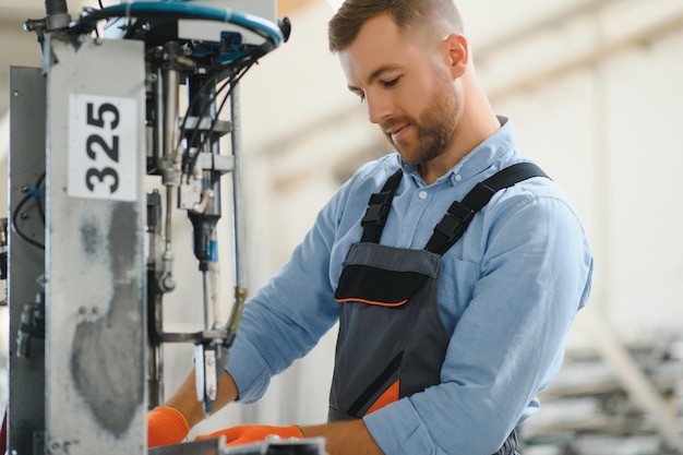 Retrato de operário em uniforme de proteção e capacete de segurança em pé pela máquina industrial na linha de produção Pessoas que trabalham na indústria