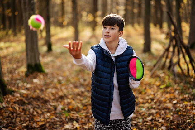 Retrato de outono ao ar livre de menino brincando com jogo de bola de pegar e jogar