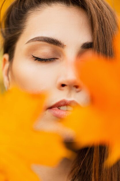 Retrato de outono aproximado de uma bela jovem com olhos fechados Rosto bonito de mulher e folhas amarelas de outono coloridas Natureza da beleza
