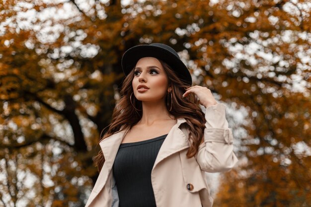 Retrato de outono de uma bela jovem glamourosa com cabelo encaracolado com chapéu vintage em um casaco elegante cinza caminhando ao ar livre com folhagem de outono colorida