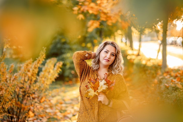 Retrato de outono de uma garota plussize com um buquê de folhas amarelas nas mãos