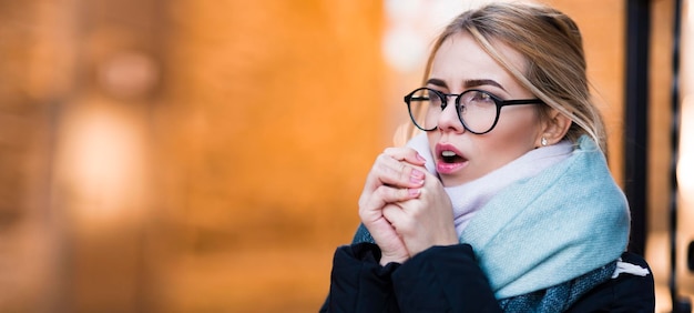 Retrato de outono de uma jovem de óculos, ela aquece as mãos com a respiração no tempo frio