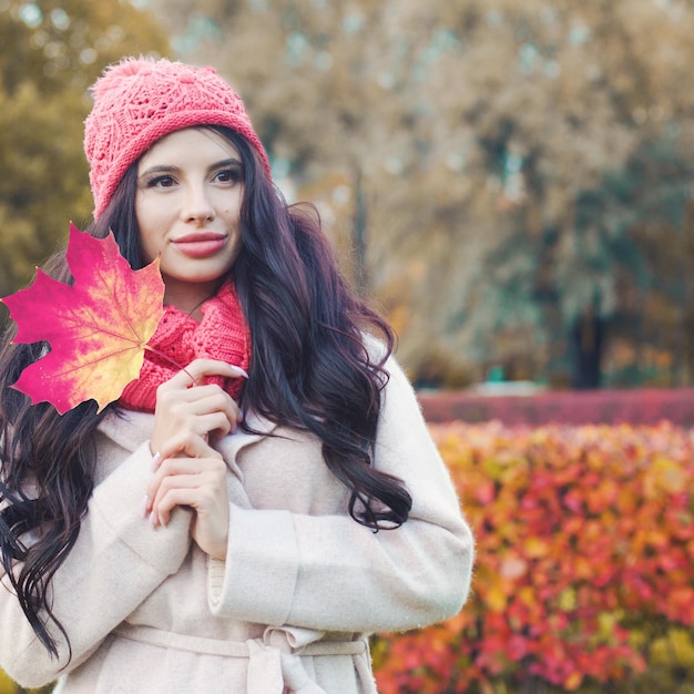 Retrato de outono de uma mulher perfeita com folha de bordo vermelha no parque de outono ao ar livre