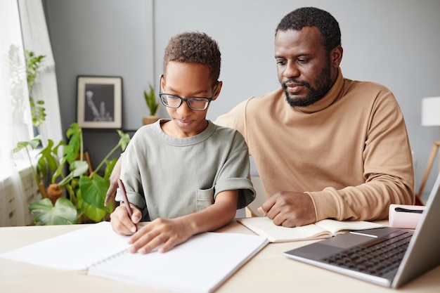 Retrato de pai afro-americano carinhoso ajudando filho com educação em casa enquanto estudava em casa, copie o espaço