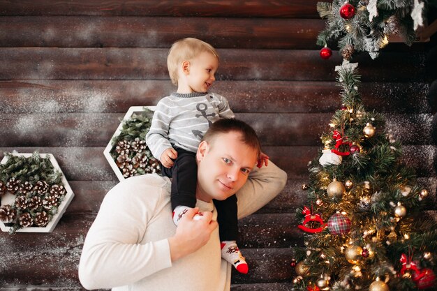 Retrato de pai amoroso com a filha nos ombros, decorando a bela árvore de Natal com brinquedos e decoração em casa