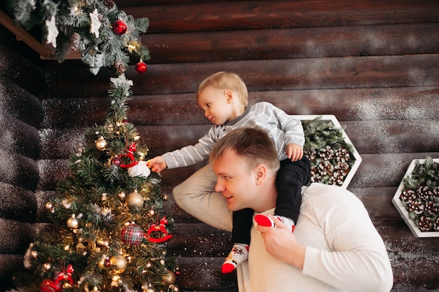 Retrato de pai amoroso com a filha nos ombros, decorando a bela árvore de Natal com brinquedos e decoração em casa