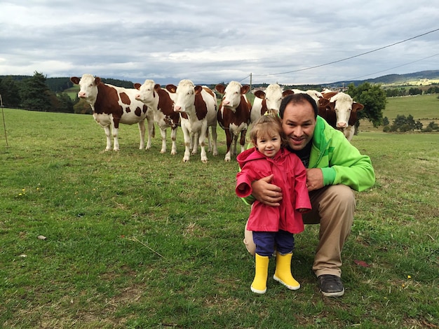 Foto retrato de pai e filha felizes com vacas em um campo gramado