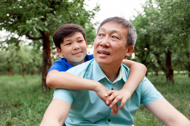 Retrato de pai velho asiático com filho pequeno ao ar livre menino coreano abraçando avô e sorrindo no parque