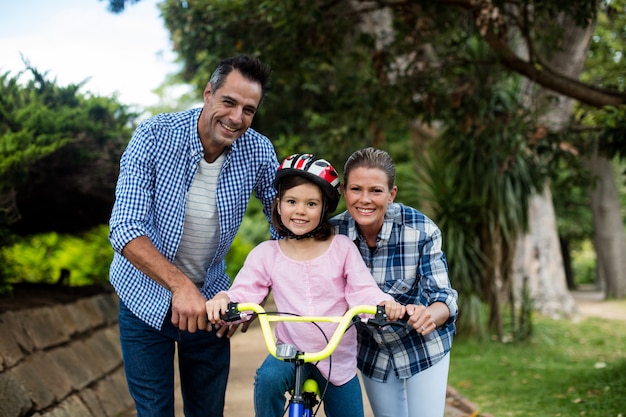 Retrato de pais felizes, ajudando a filha a andar de bicicleta no parque