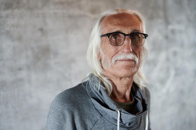 Retrato de pensionista de homem caucasiano de cabelos grisalhos envelhecido em copos. Vovô legal com bigode e rosto amigável sorridente, olhando para a câmera no fundo cinza