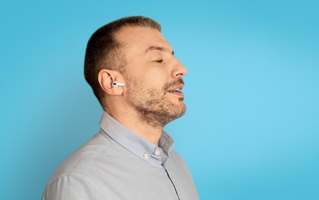 Retrato de perfil de homem ouvindo música usando fones de ouvido fundo azul