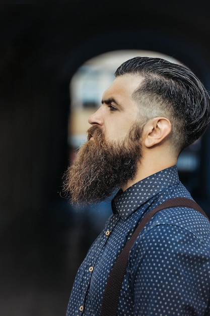 Retrato de perfil de jovem barbudo bonito com barba longa e bigode tem penteado elegante em camisa ao ar livre