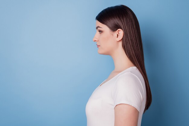 Retrato de perfil de senhora encantadora, linda e calma olhando o espaço vazio posando sobre fundo azul