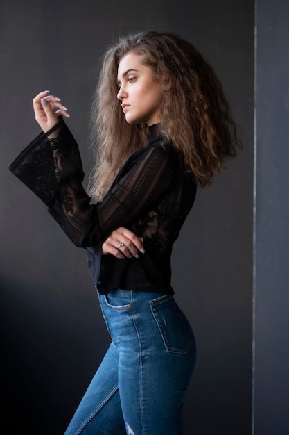 Retrato de perfil de uma jovem vestida com uma mala preta e jeans sobre fundo cinza