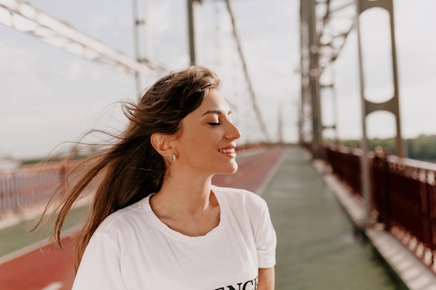 Retrato de perfil de uma mulher adorável em camiseta branca passando tempo ao ar livre