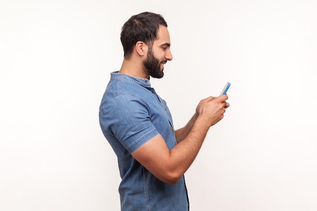 Retrato de perfil homem barbudo feliz conversando no smartphone e sorrindo, correspondência de prazer, aplicativo de namoro. Tiro de estúdio interior isolado no fundo branco