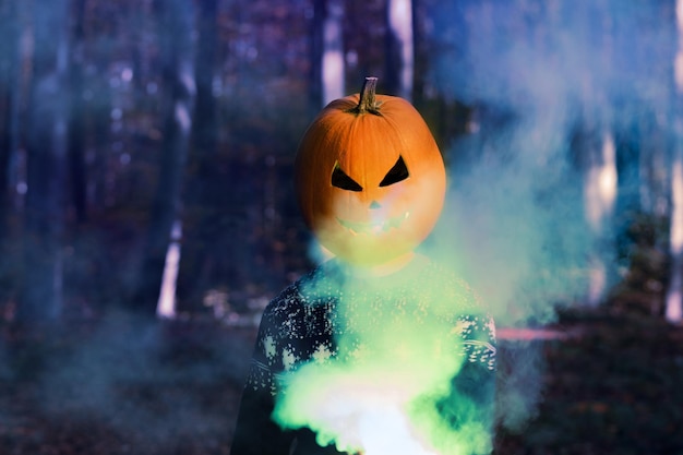 Retrato de pessoa adulta com abóbora de Halloween na cabeça em uma noite de floresta com fumaça colorida Halloween Jackolantern festa engraçada