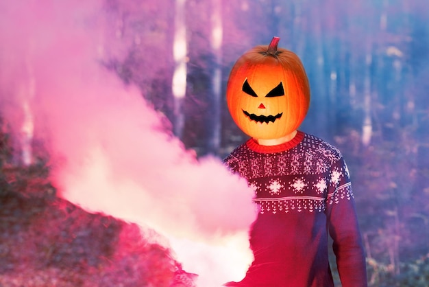 Retrato de pessoa adulta com abóbora de Halloween na cabeça em uma noite de floresta com fumaça colorida