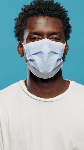 Retrato de pessoa casual usando máscara facial e olhando para a câmera. Feche o jovem com máscara protetora contra a pandemia de coronavírus em pé sobre fundo isolado no estúdio.