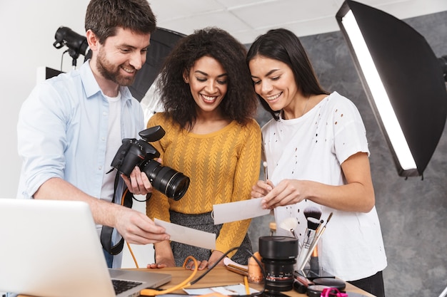 Retrato de pessoas alegres e multiétnicas, homem e mulher, olhando para um laptop durante a sessão de fotos com uma câmera profissional no estúdio