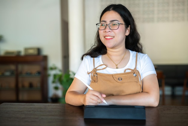 Retrato de pessoas freelance asiáticas de negócios feminino usando óculos elegante hipste Desenhe ou tome nota no tablet digital com caneta eletrônica para navegar na internet conversando e blogando no café