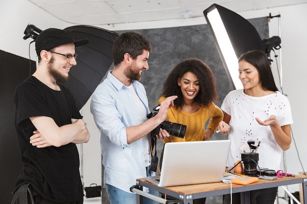 Foto retrato de pessoas modernas e multiétnicas, homens e mulheres, olhando para um laptop durante a sessão de fotos com uma câmera profissional em estúdio