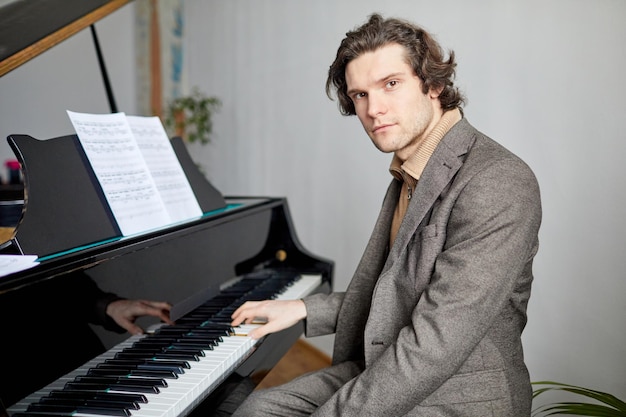 Retrato de pianista profissional de terno olhando para a câmera enquanto toca notas no piano na escola musical