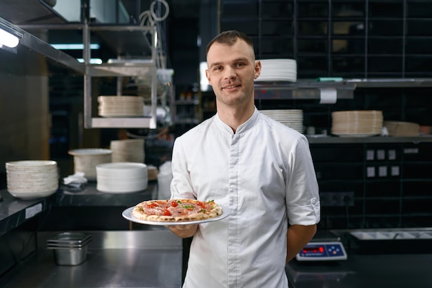 Retrato de pizzaiolo masculino apresentando pizza recém cozida. Master class da escola de culinária ou apresentação de restaurante italiano de fast food