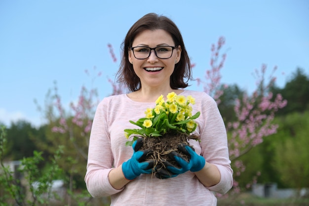 Retrato de primavera de fêmea em luvas com flores de prímula nas mãos no jardim