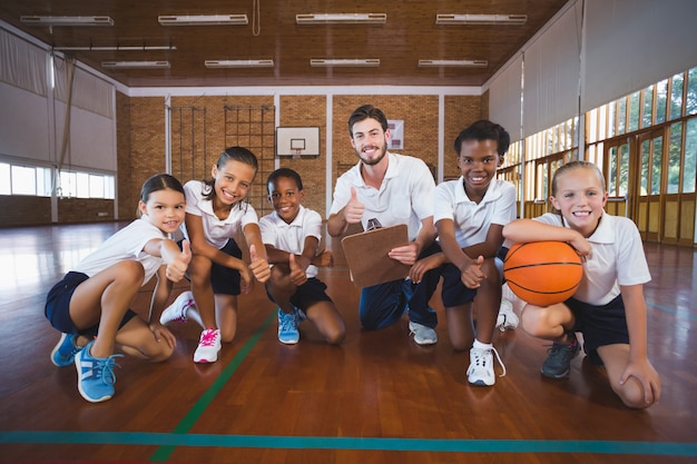 Retrato de professor de esportes e crianças da escola na quadra de basquete