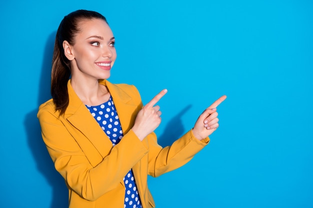 Retrato de promotor positivo de menina alegre apontar o dedo indicador copyspace demonstra anúncios promo usar jaqueta blazer isolada sobre fundo de cor azul