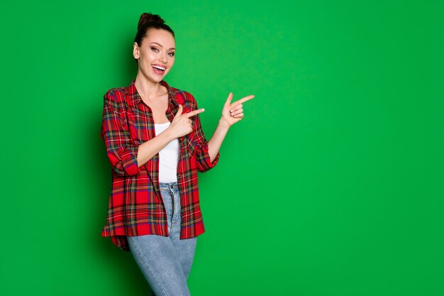 Retrato de promotor positivo de menina alegre indica anúncio ponto de promoção dedo indicador copyspace usar jeans isolado brilho cor de fundo