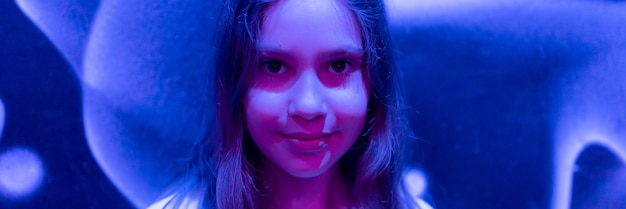 Foto retrato de rosto fofo, feliz e cândida pré-adolescente caucasiana de nove anos de idade no estúdio iluminado por faixa de luz neon roxa azul