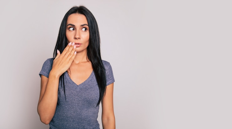Foto retrato de rosto inteiro de uma senhora encantadora, que está olhando para a câmera com os olhos bem abertos e cobrindo a boca com os dedos de ambas as mãos