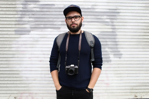 Retrato de rua de um fotógrafo masculino com barba de óculos e um boné com uma câmera fotográfica vintage