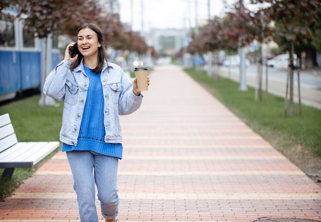 Retrato de rua de uma jovem alegre falando ao telefone com café na mão copie o espaço