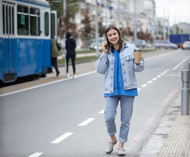 Retrato de rua de uma jovem alegre falando ao telefone com café na mão