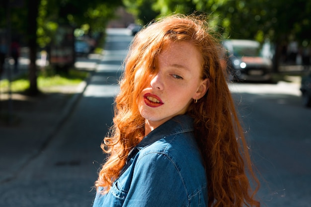 Retrato de rua de uma mulher ruiva atraente com camisa jeans em raios de sol na rua