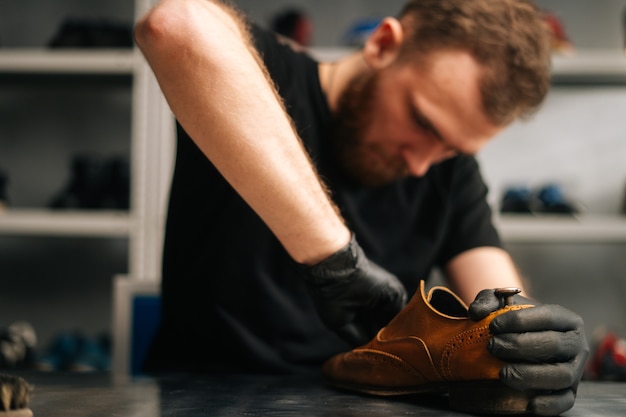 Retrato de sapateiro barbudo limpando sapatos de couro velhos para restauração posterior.